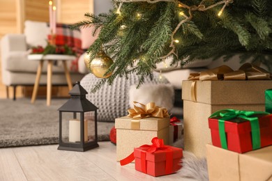 Photo of Gift boxes under Christmas tree and lantern with candle indoors