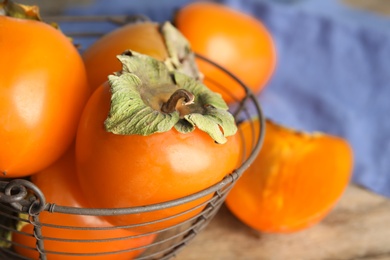 Delicious fresh persimmons in metal basket on table, closeup