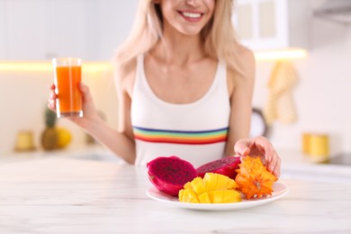 Photo of Woman with fresh juice and exotic fruits at table in kitchen, closeup
