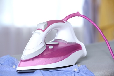 Modern electric iron and clean shirt on board indoors, closeup