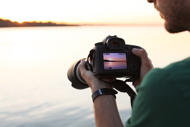 Male photographer holding professional camera with photo of riverside sunset on display