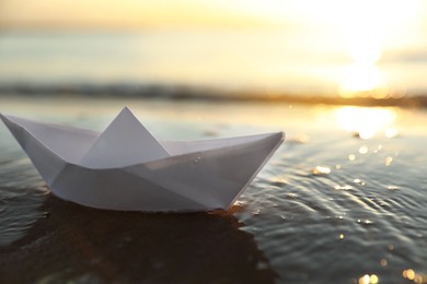 White paper boat in shallow water of sea at sunset, space for text