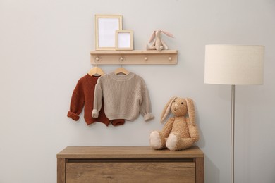 Children's room interior with stylish wooden furniture, baby clothes and lamp