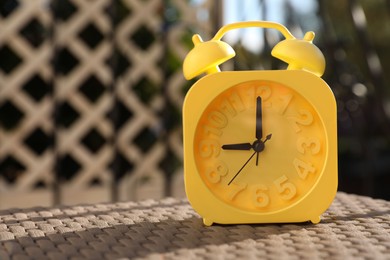 Yellow alarm clock on table outdoors at sunny morning. Space for text