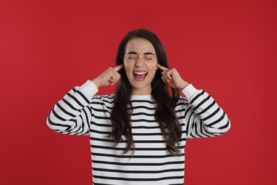 Emotional young woman covering ears with fingers on red background