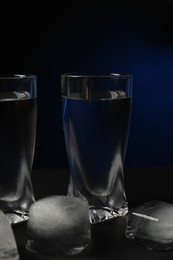 Shot glass of vodka with ice cubes on black table against dark background, closeup
