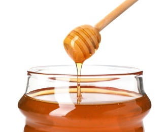 Honey dripping from dipper into jar on white background