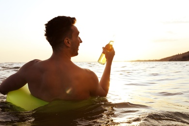 Young man with drink on inflatable ring in sea