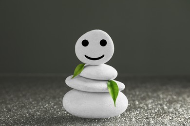 Stack of stones with drawn happy face and green leaves on grey background. Zen concept