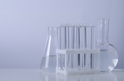 Photo of Different laboratory glassware with transparent liquid on table against light background. Space for text