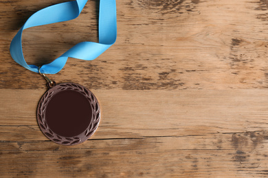 Bronze medal with light blue ribbon on wooden background, flat lay. Space for design