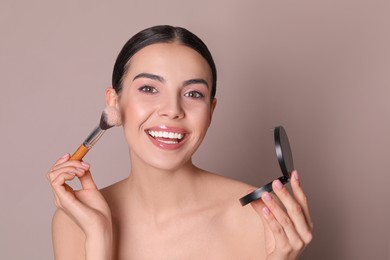 Photo of Beautiful young woman applying face powder with brush on dusty rose background