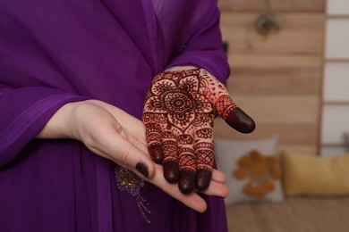 Woman with henna tattoo on palm indoors, closeup. Traditional mehndi ornament