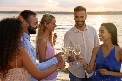 Friends with glasses of wine having fun near river at summer party