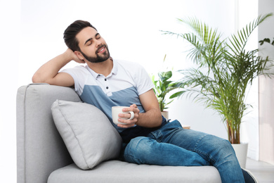 Young man with cup of drink relaxing on couch at home
