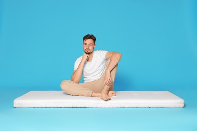 Man sitting on soft mattress against light blue background