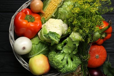 Photo of Different fresh vegetables in wicker basket on black wooden table, top view. Farmer harvesting
