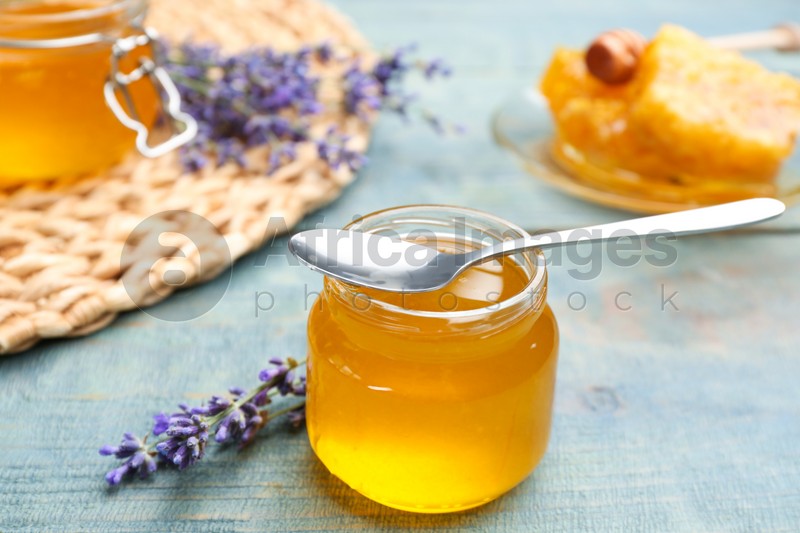 Tasty honey in glass jar and lavender flowers on light blue wooden table