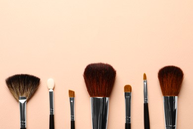 Different makeup brushes on light beige background, flat lay . Space for text