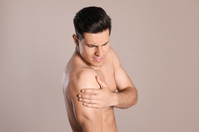 Man suffering from shoulder pain on beige background