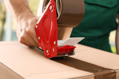 Man packing box with adhesive tape indoors, closeup. Moving service