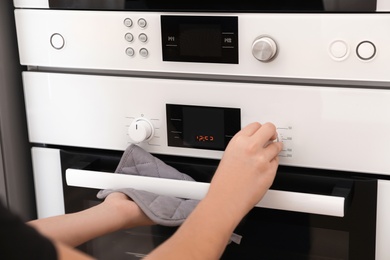 Photo of Woman adjusting electric oven in kitchen, closeup