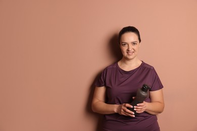 Happy overweight woman with bottle of water on pale pink background, space for text