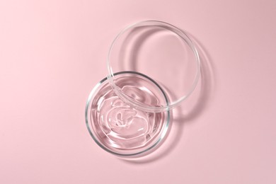 Petri dish with liquid and lid on pale pink background, flat lay