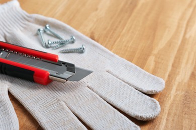 Utility knife, screws and glove on wooden table, closeup. Space for text