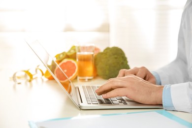 Nutritionist working with laptop at desk in office, closeup