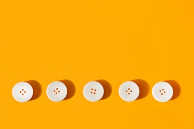 Line of white buttons on orange background, flat lay. Space for text