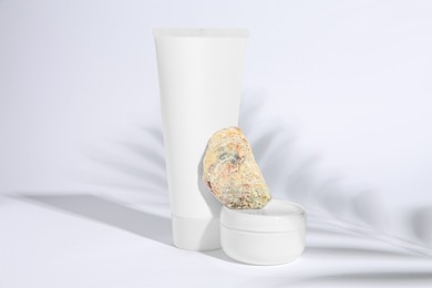 Photo of Cosmetic products, quartz gemstone and shadow of tropical leaf on white background