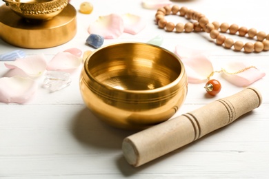 Composition with golden singing bowl and mallet on white wooden table. Sound healing