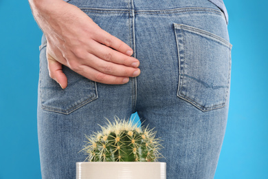 Man sitting down on cactus against light blue background, closeup. Hemorrhoid concept