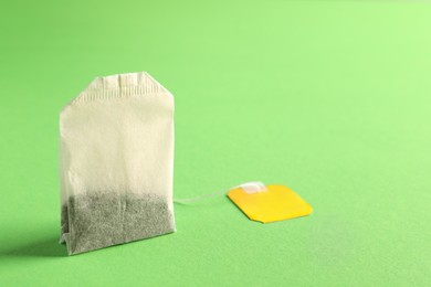 New tea bag with tab on green background, closeup. Space for text