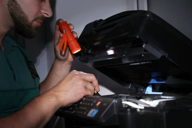 Repairman with flashlight fixing modern printer indoors, closeup