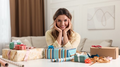 Young woman with beautifully wrapped gifts at table in living room