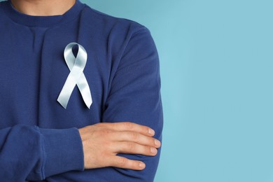 Photo of Closeup view of man with ribbon on light blue background, space for text. Urology cancer awareness