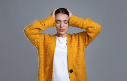 Young woman suffering from headache on grey background. Cold symptoms