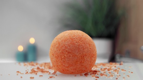 Orange bath bomb with salt on countertop near tub indoors, closeup. Bokeh effect