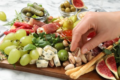 Photo of Woman taking pistachio from board with different appetizers at white table, closeup