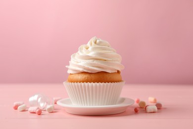 Delicious cupcake decorated with cream on pink wooden table