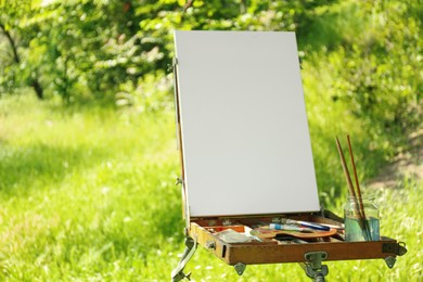 Easel with blank canvas and painting equipment in countryside