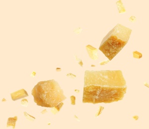 Pieces of delicious parmesan cheese flying on beige background