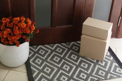 Cardboard boxes on stylish door mat and beautiful flowers near entrance