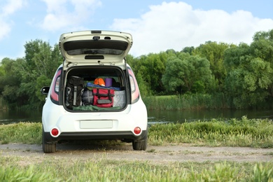 Car with camping equipment in trunk on riverbank. Space for text