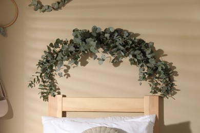 Beautiful garland made of eucalyptus branches hanging on light olive wall in bedroom