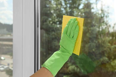 Woman cleaning window glass with sponge cloth indoors, closeup