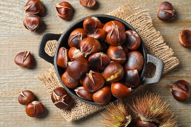 Tasty roasted edible chestnuts on wooden table, flat lay