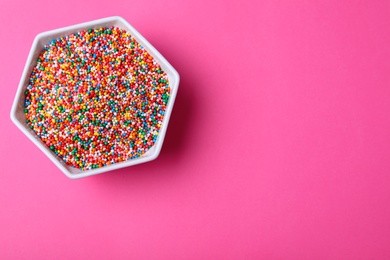 Colorful sprinkles in bowl on pink background, top view with space for text. Confectionery decor